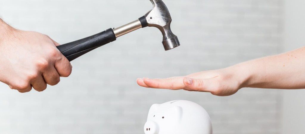 A hand holding a hammer which is raised above a white piggy bank