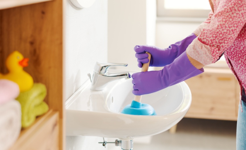 Woman unclogging the bathroom sink using a plunger
