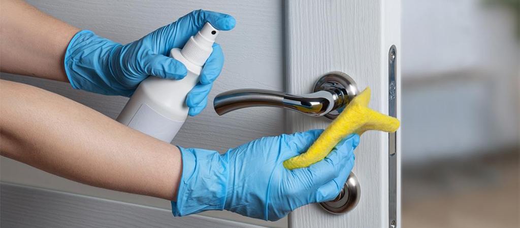 Gloved hands of woman disinfecting door handle
