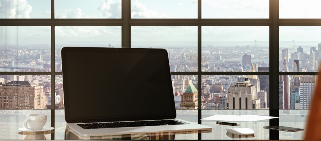 Blank laptop on a glass table in a modern office and city views from the windows