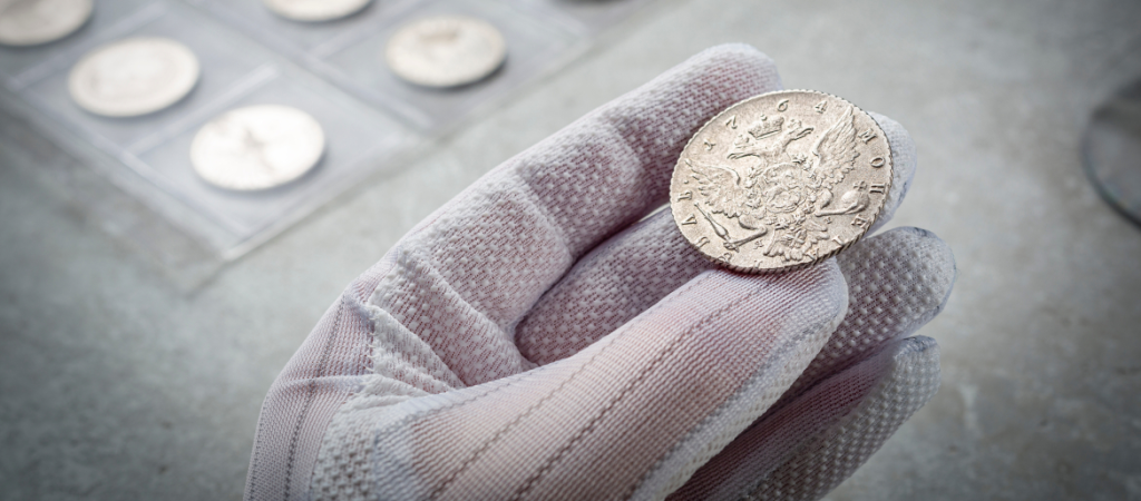 hand wearing glove holding a decorated coin in front of a coin collection