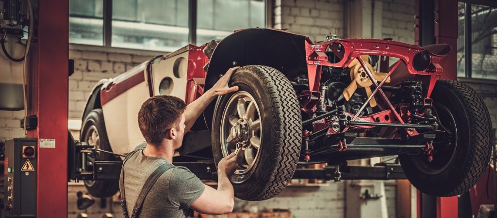 Mechanic Working on Classic Car Wheels and Suspension in Restoration Workshop
