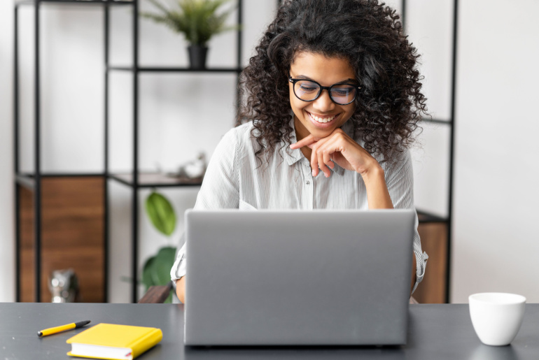 Portrait of a young African American woman with Afro hairstyle in glasses sitting at the desk with a laptop