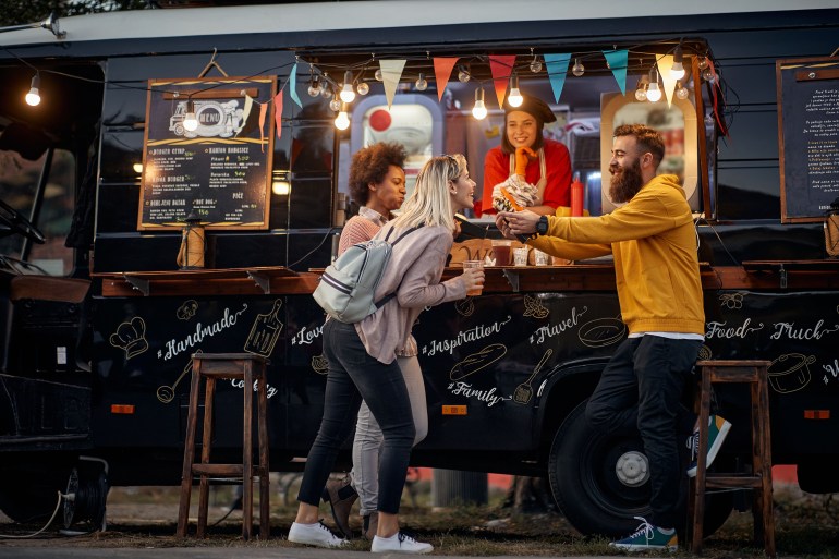 group of multiethnic young people having fun while eating in front of modified truck for mobile fast food service