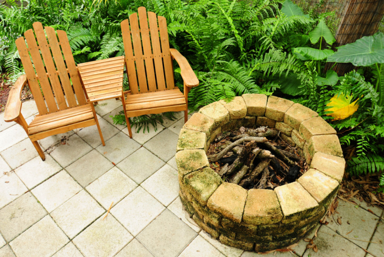 Adirondack chairs on a relaxing patio with a fire pit and green plants