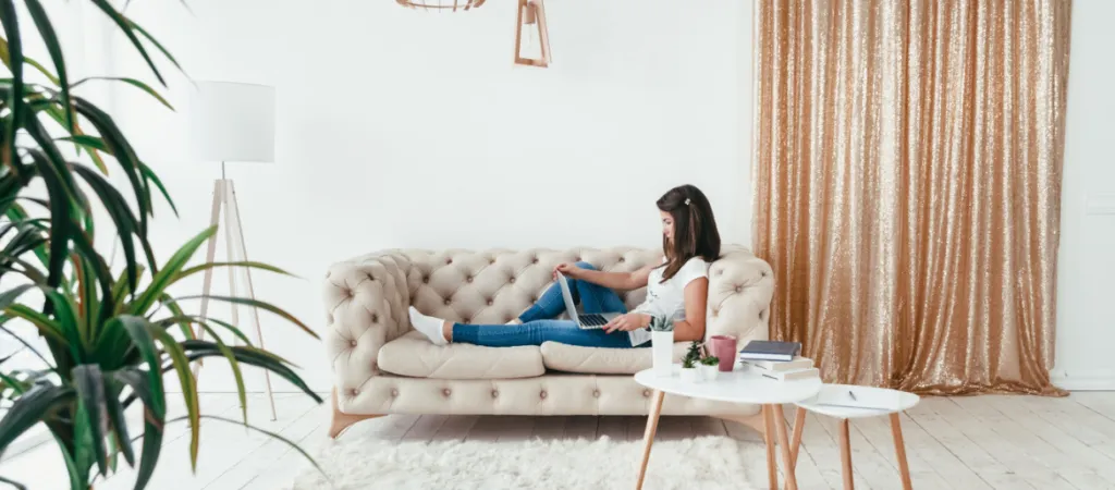 young woman working from home on a laptop lying on the sofa in the room