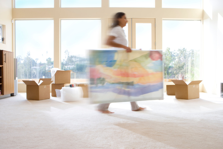 Action shot of woman carrying painting into new home on moving day, piece of art