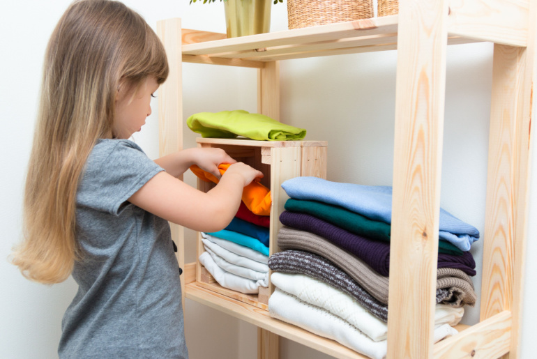 The girl is measuring her mother's clothes and shoes. Order in the closet. Smart storage system. Capsule wardrobe. The girl plays and puts mother's clothes in order or chaos. Wardrobe order.