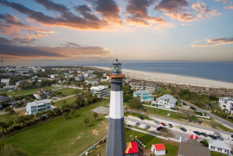 Tybee Island Beach with the lighthouse, blue ocean water, a brown sandy beach, homes and lush green trees and grass in Tybee Island Georgia USA