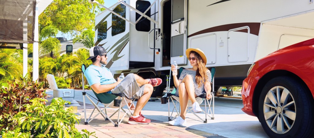 Young couple sits near camping trailer, smiling