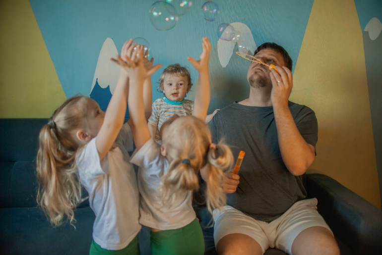 adult with many children has fun blowing soap bubbles