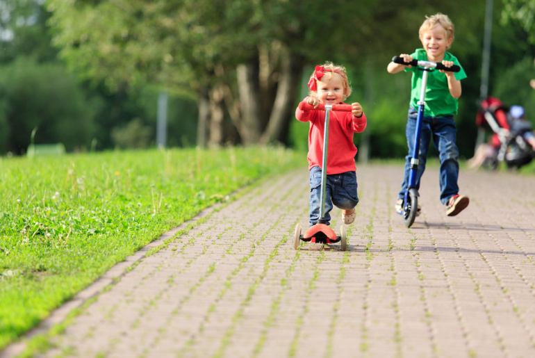 little boy and toddler girl riding scooters in summer park, kids sport baby gifts