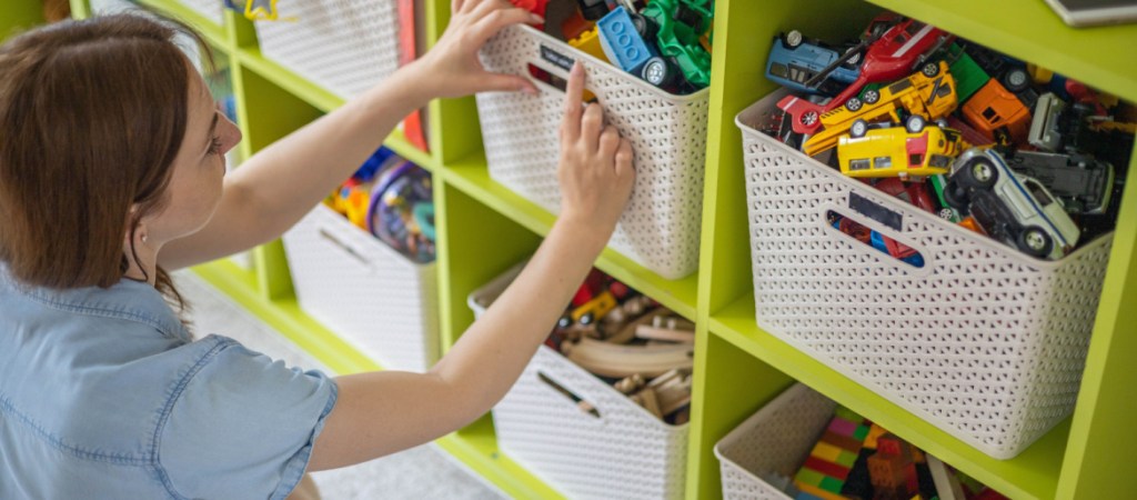 Woman hands applying printing sticker with name title of children toys for comfortable sorting and storage at home. Caring mother organizing domestic space for kids. Housekeeping and household