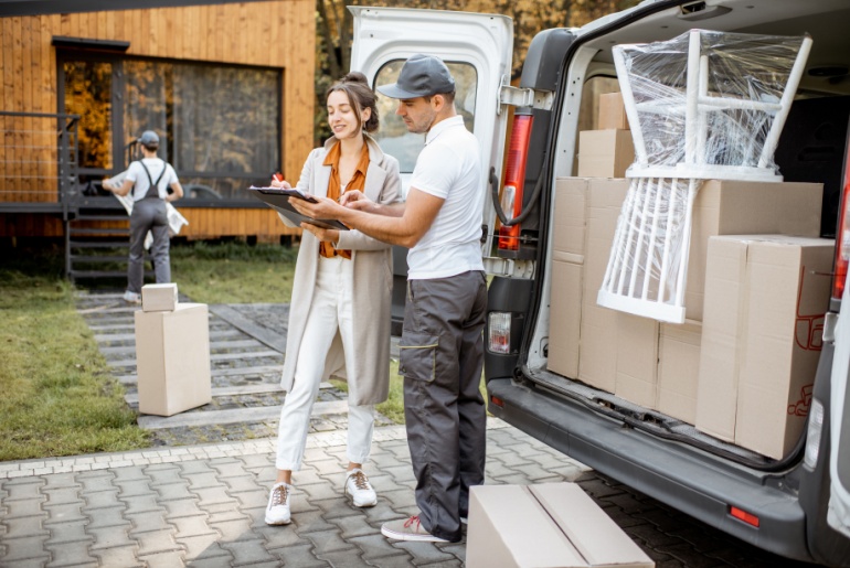 Delivery company employees unloading goods from a car trunk, delivering goods to a woman's home.