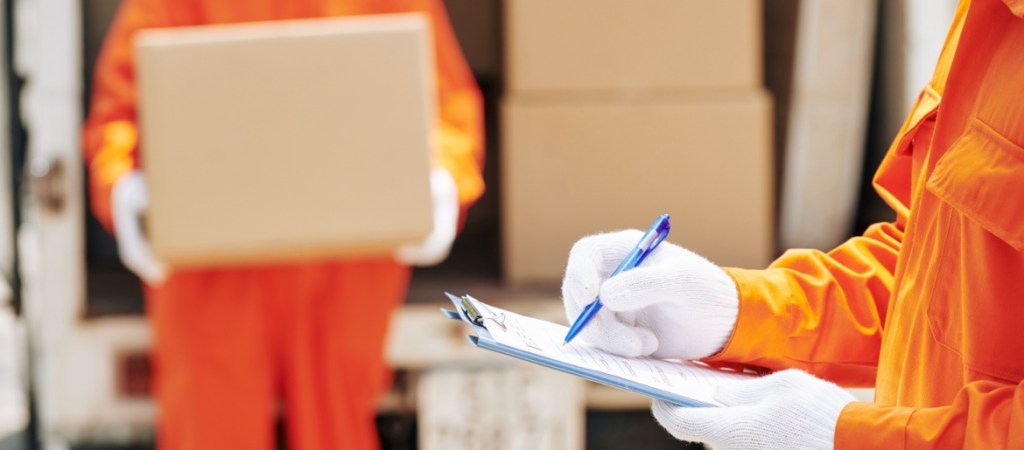 Moving man wearing orange uniform and white gloves holding clipboard with checklist paper making notes