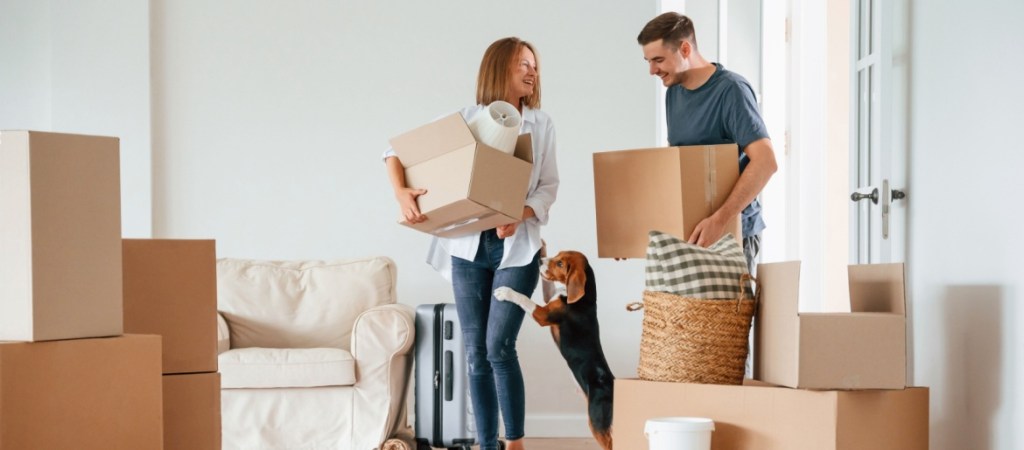 Two boxes in hands. Young couple with dog are moving to new home