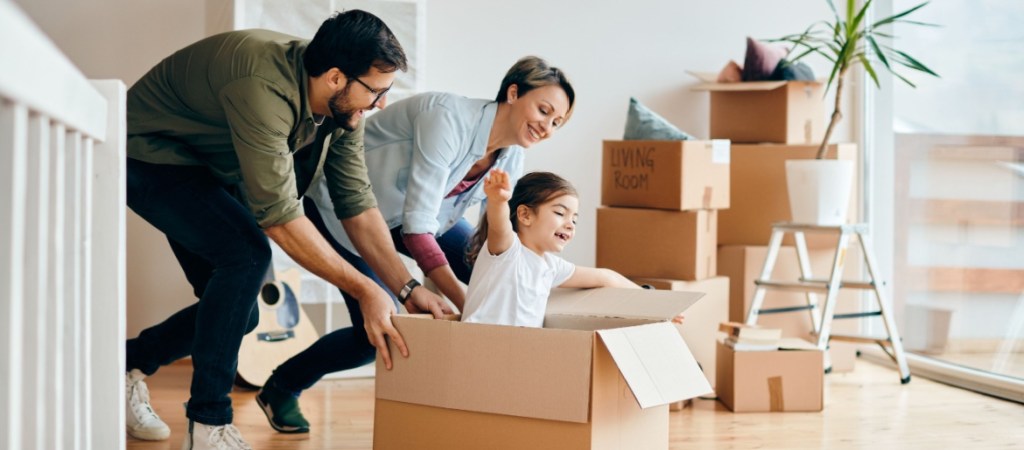 Happy-parents-having-fun-with-their-daughter-while-pushing-her-in-carton-box-at-their-new-home