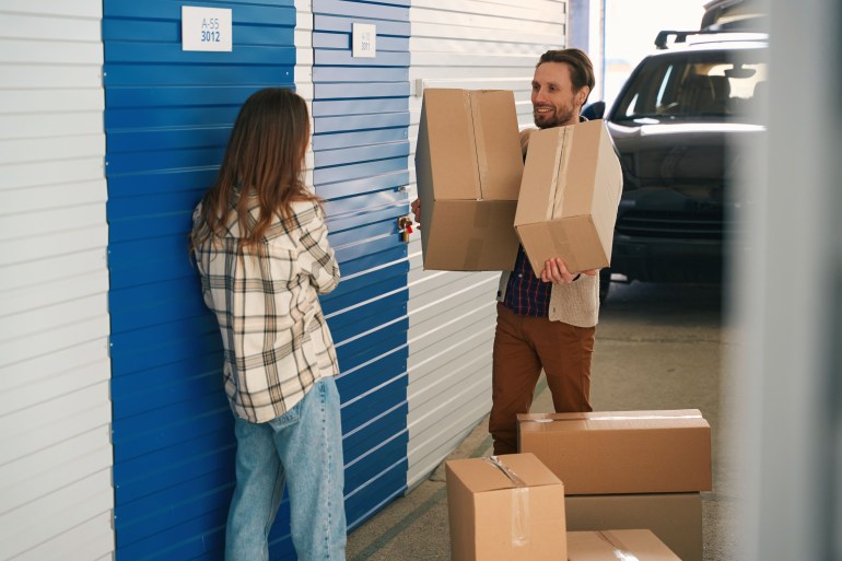 Man and lady with big cardboard boxes in front of self storage unit