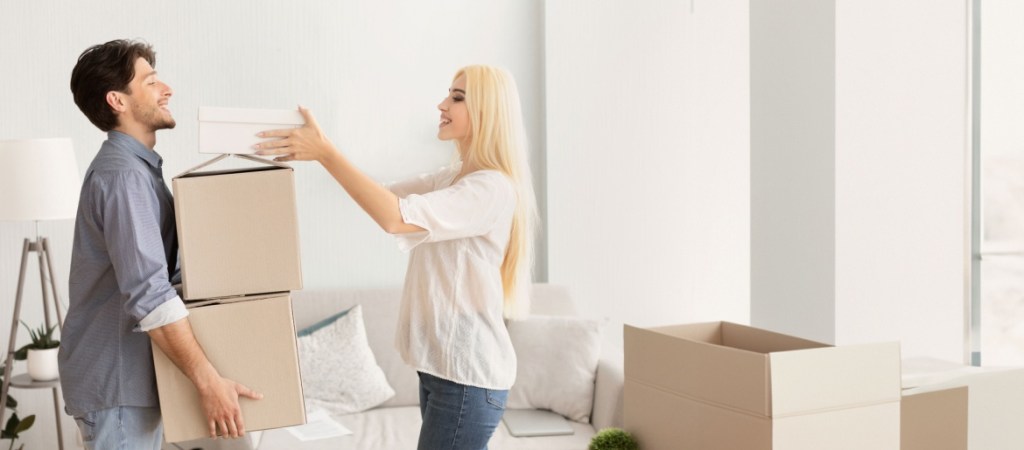 A cheerful couple is unpacking cardboard boxes in their bright living room. They are enjoying the moment as they organize their new home together