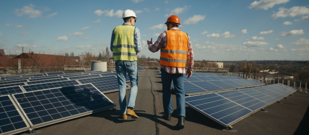 Full-shot-of-engineer-and-technician-discussing-on-flat-roof-between-solar-panels