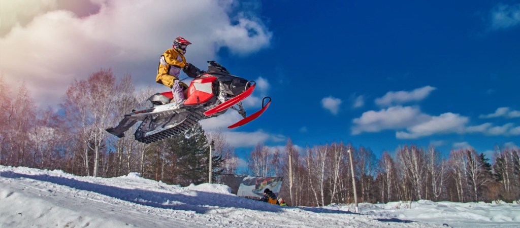Snowmobile in high jump above track on sunny day.