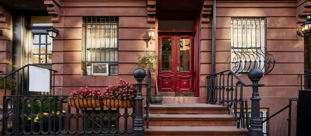 A bright red door and colorful flowers on a brownstone in a neighborhood of Manhattan, New York City.