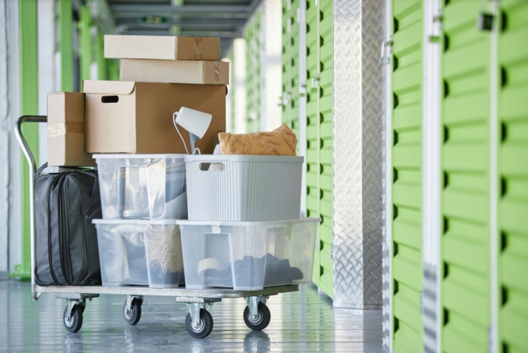 cardboard and plastic boxes storing personal belongings loaded on dolly cart next to self storage unit