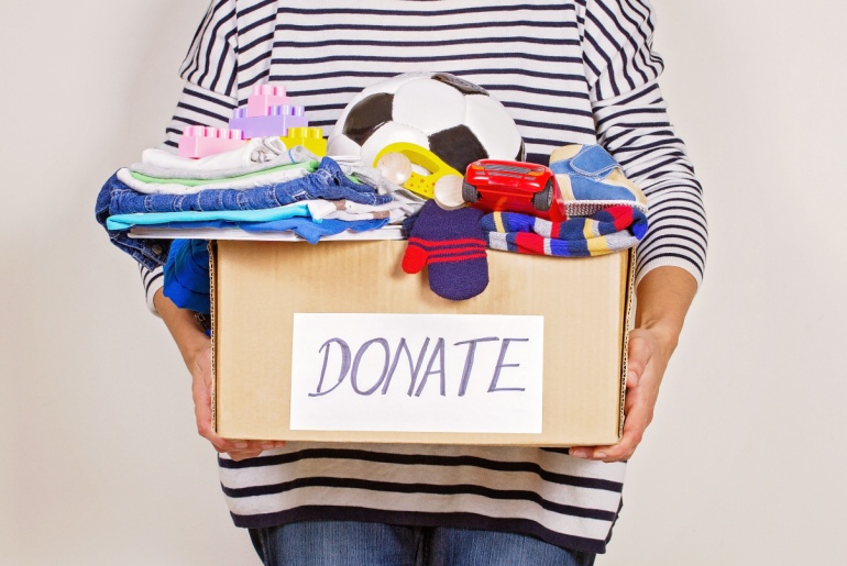 Woman hand holding donation box with clothes, toys and books for charity