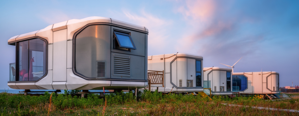 Modern Modular Tiny Houses in a Field. Alternative housing units with wind turbines in the distance at sunset
