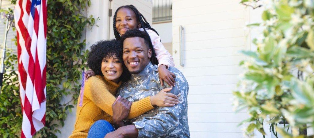 Military spouse and husband hugging with child behind them.