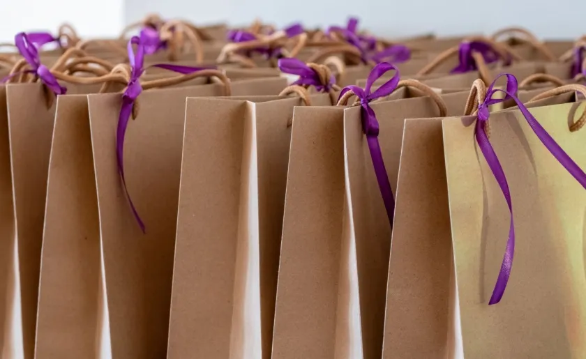Close-up of brown paper gift bags tied with purple ribbons.