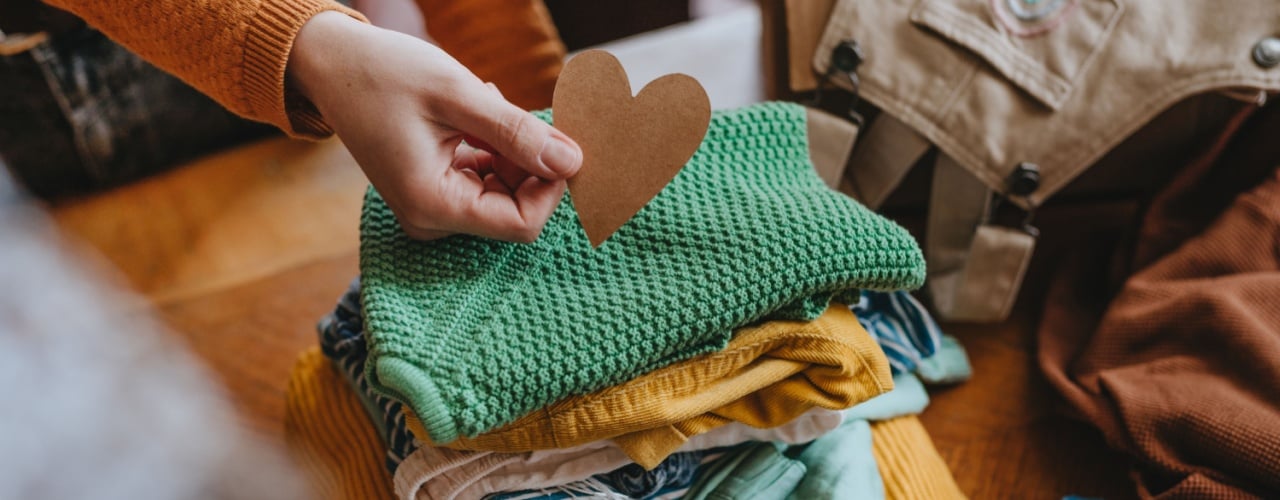 Woman holding a paper heart near old out-of-use kid clothes for donations.