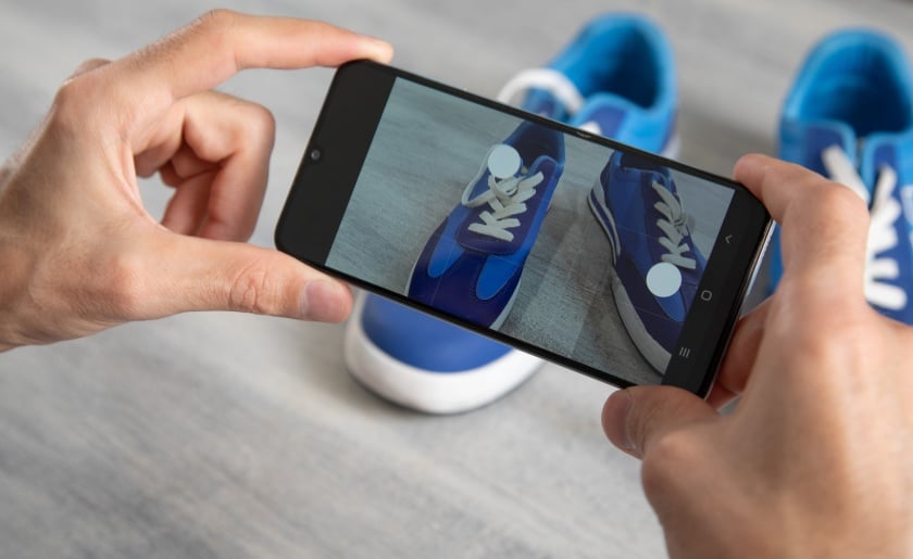 Man taking a picture with a smartphone of sports shoes.