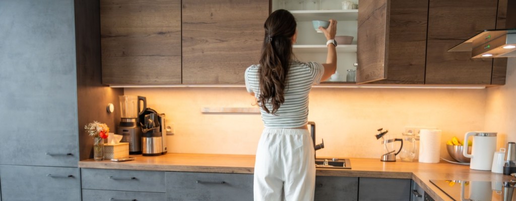 Woman putting cup in kitchen cabinet.