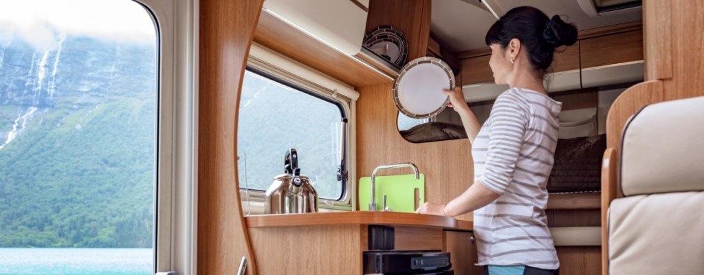 Woman in RV putting dishes away in cabinet.