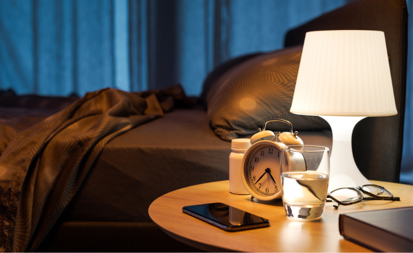 Personal items, lit lamp and medicines on the bedside table in a guest room
