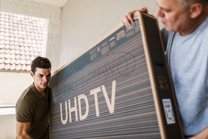Two people moving a TV packed in its box