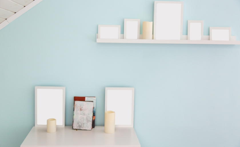 white shelf and a table with white frames for photos, beige candles and books in the attic guest room