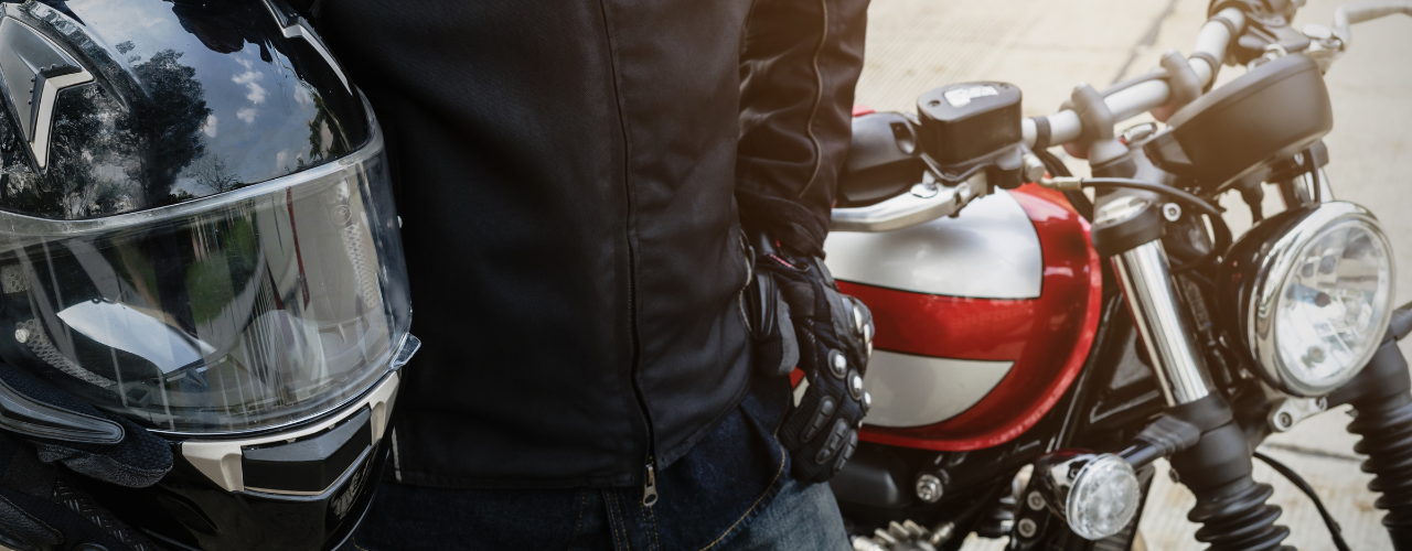 Biker wearing jacket suit holding helmet with motorcycle.
