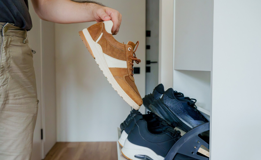 Side view of a man taking a pair shoes from an open white tilting shoe cabinet in a modern hallway